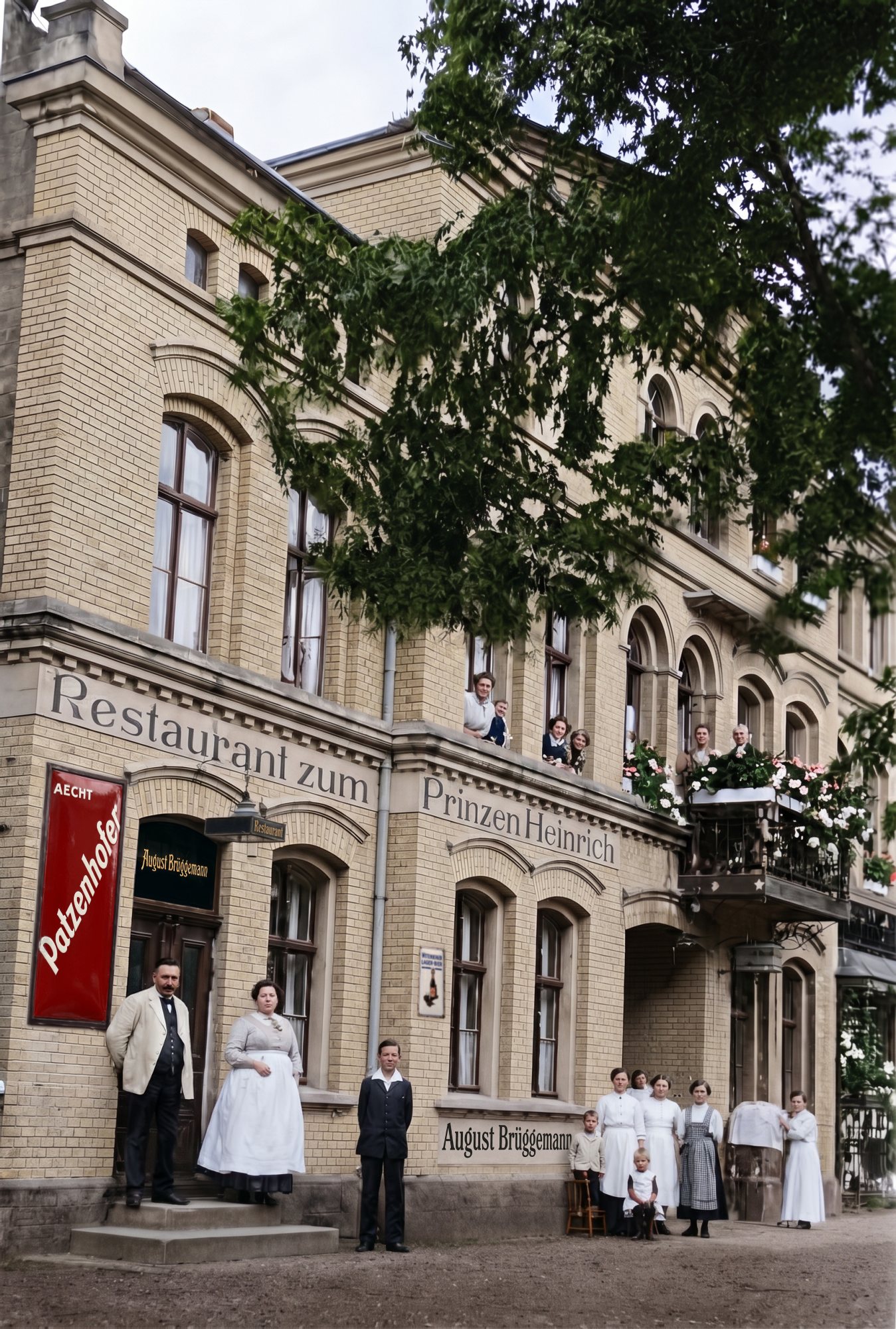 Das Restaurant zum Prinzen Heinrich von der Straße aus: die Wirtsleute vor der Tür, Personal neben der Hofeinfahrt, Gäste an den Fenstern und auf dem Balkon mit Blumenkästen, darüber eine große Linde