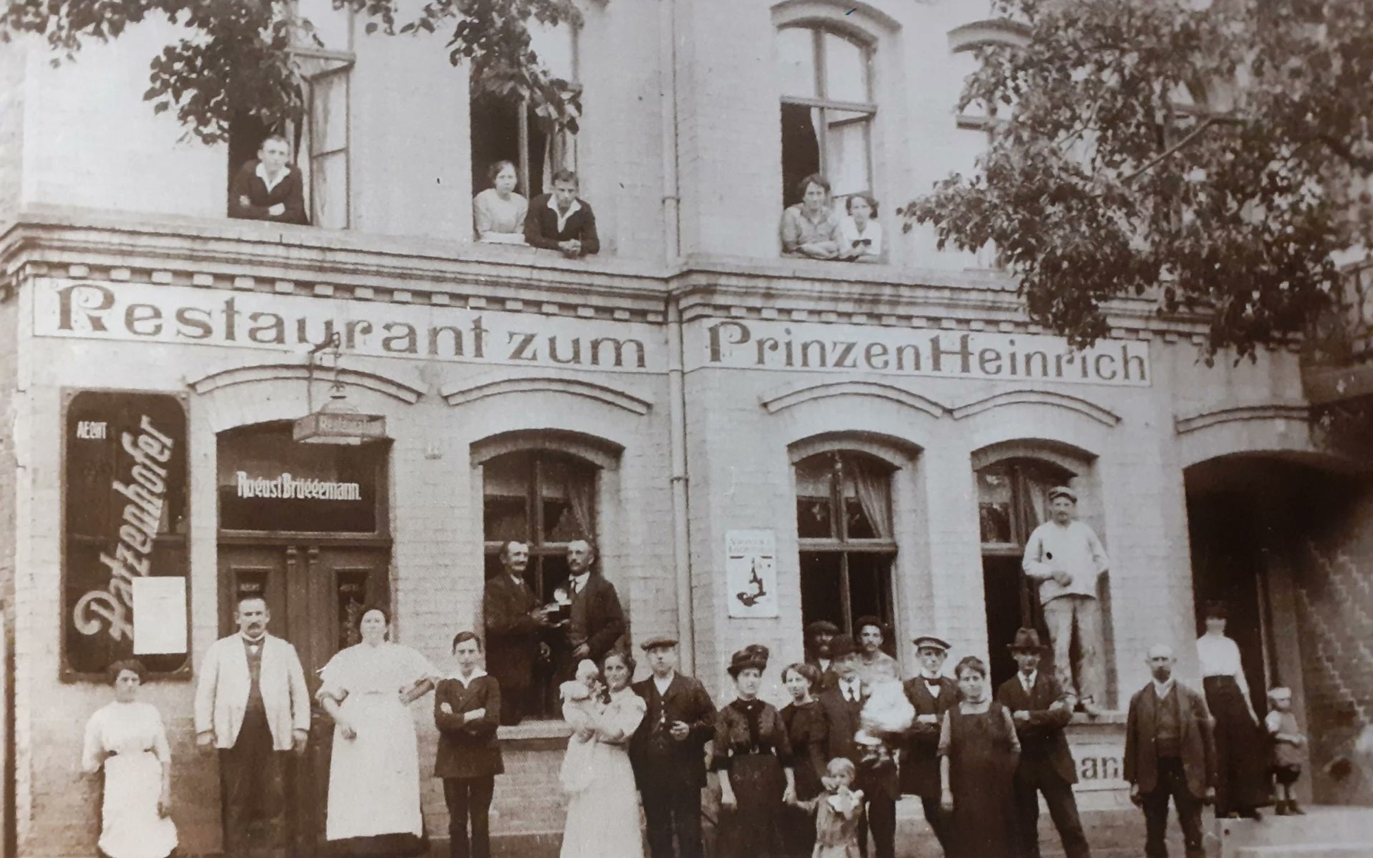 Wirtsfamilie, Personal und Gäste vor dem Restaurant zum Prinzen Heinrich, um 1910. Über der Tür der Name August Brüggemann, links ein Schild für Aecht Patzenhofer, in den Fenstern oben weitere Bewohner.