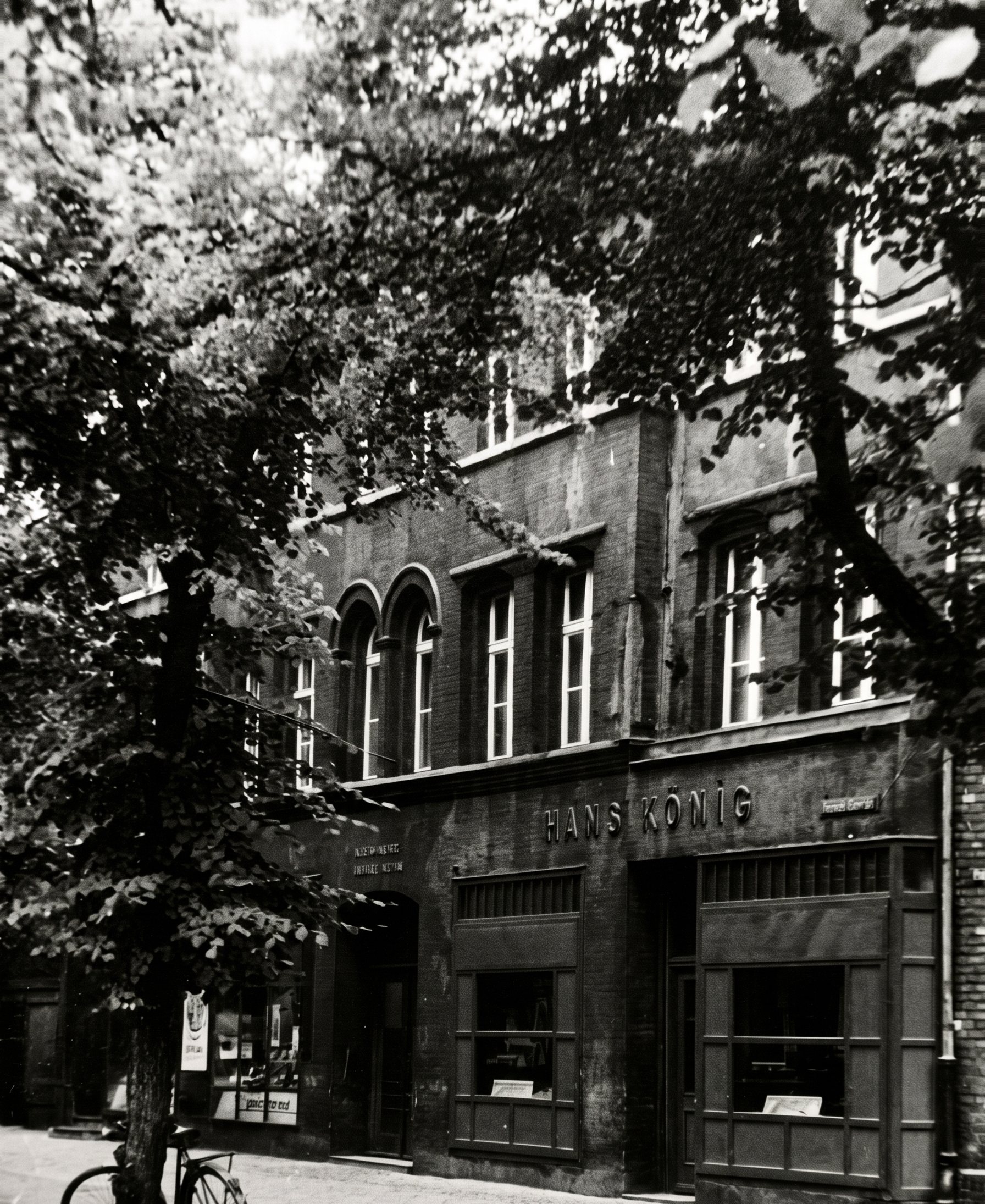Die Fassade um 1969, dunkel und unrenoviert, unten zwei Läden, rechts der Schriftzug Hans König, links ein Fahrrad
