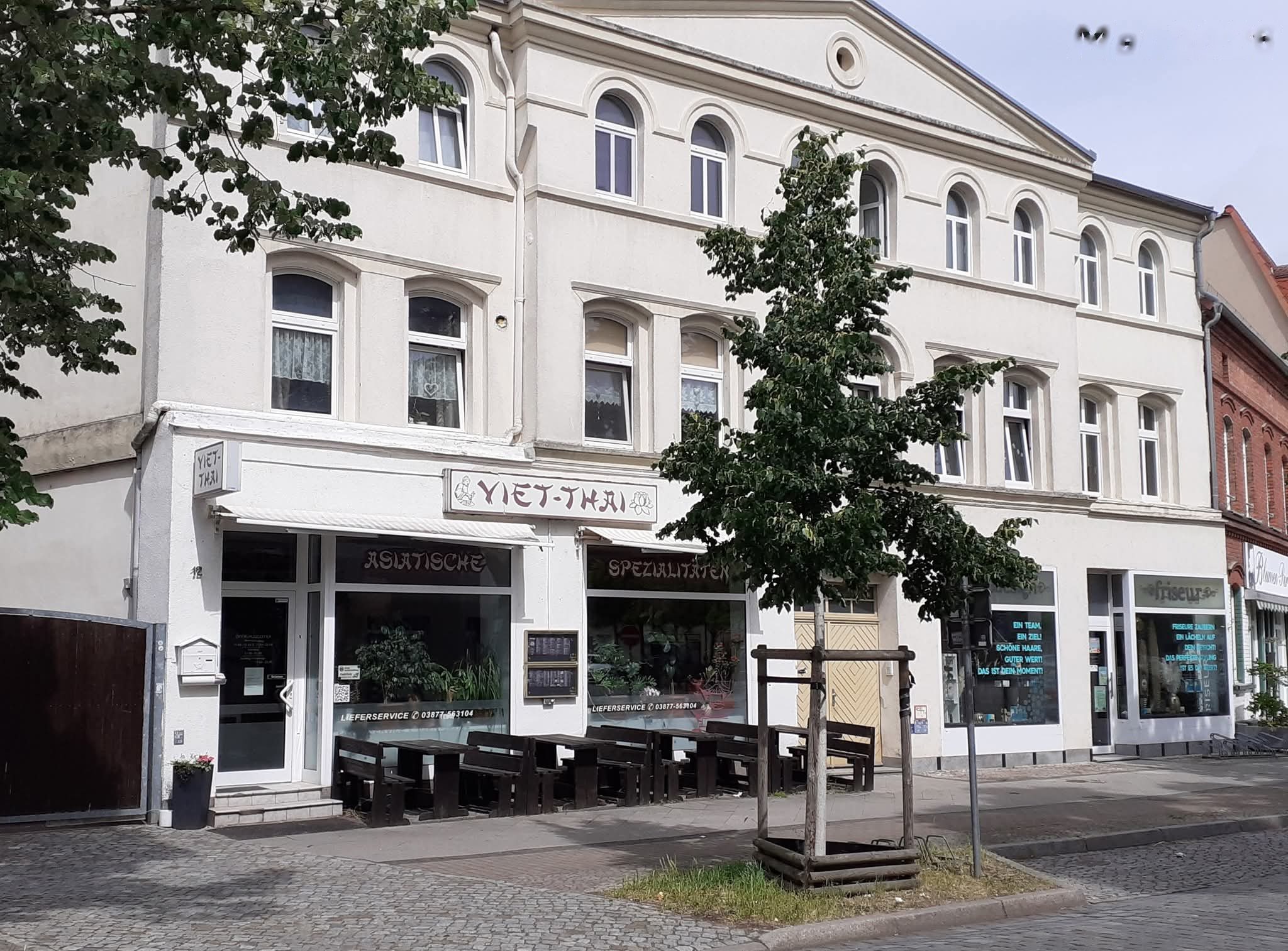 Das Haus Friedrich-Ebert-Straße 12 mit dem Schild Viet-Thai über den Schaufenstern und Tischen davor, links das dunkle Tor zum Hof